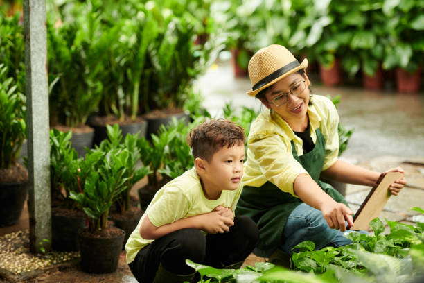 Unleashing the Power of Cooperative Gardening: Empower Your Neighborhood Today! mother working at flower nursery and teaching son how to define plants